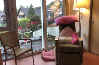 Sessel mit pinken Kissen und Lampe vor regennasser Balkontür