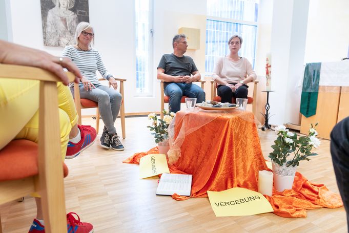 Teilnehmende sitzen im Stuhlkreis um orange gedeckten Tisch mit Karte VERGEBUNG
