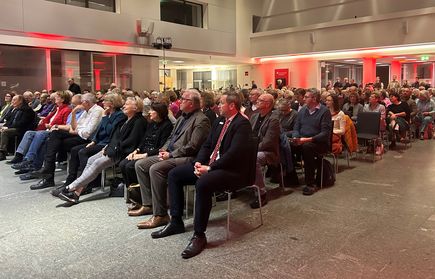 Großes Publikum sitzt in modernem Saal mit roter Beleuchtung