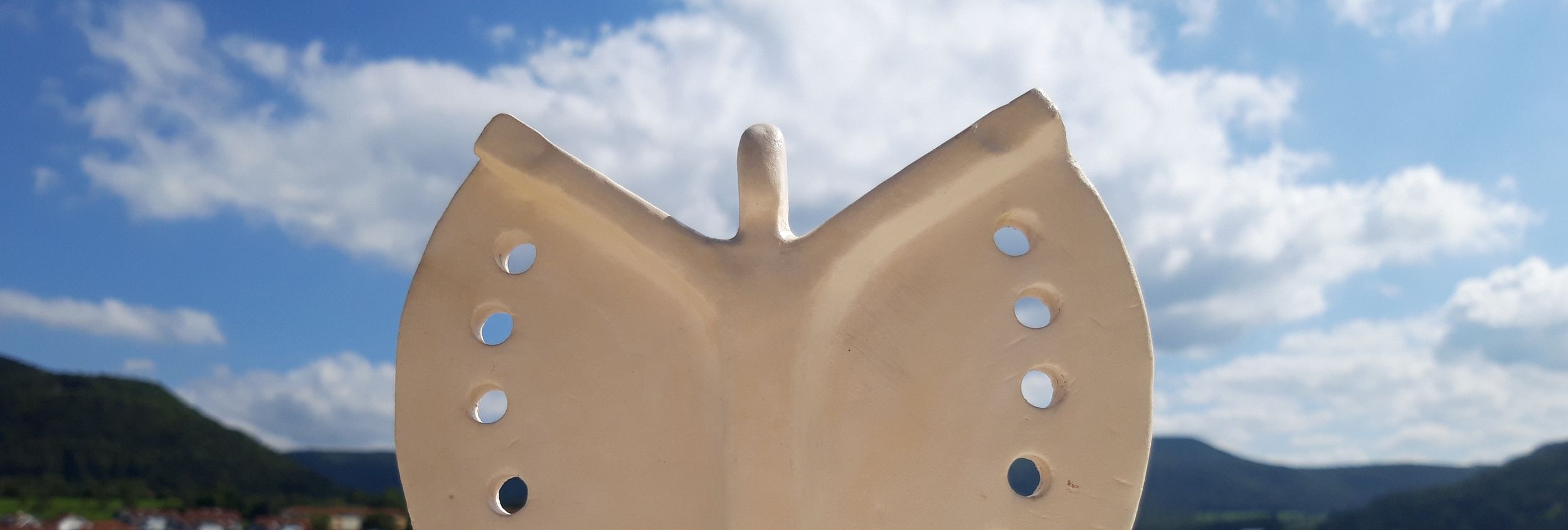 Beiges Keramikschmetterlingsornament mit runden Löchern vor blauem Himmel