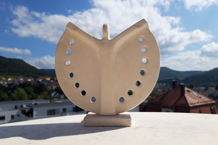 Beiges Keramikschmetterlingsornament mit runden Löchern vor blauem Himmel