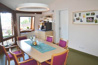 Gemeinschaftsraum mit langem Tisch violetten Stühlen und runder Hängeleuchte