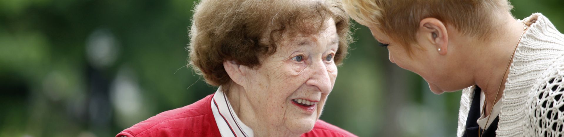 Ältere Frau in roter Weste lächelt jüngere Frau beugt sich zu ihr