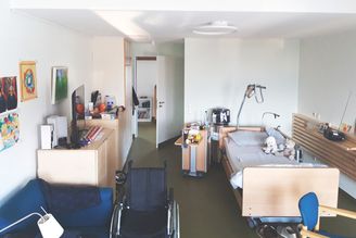 Pflegezimmer mit elektrisch verstellbarem Bett Rollstuhl und Kuscheltieren