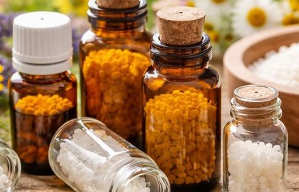 Kleine Glasfläschchen mit weißen und gelben Pellets vor Kamillenblüten