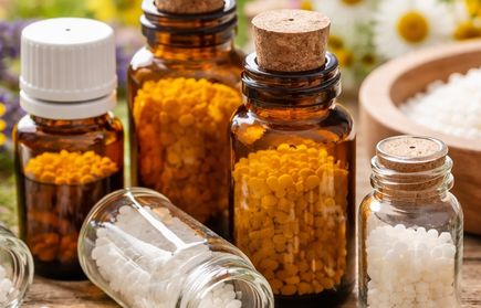 Kleine Glasfläschchen mit weißen und gelben Pellets vor Kamillenblüten