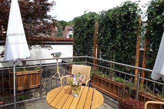 Balkon mit rundem Holztisch, Vase mit rosa Blumen und Efeu