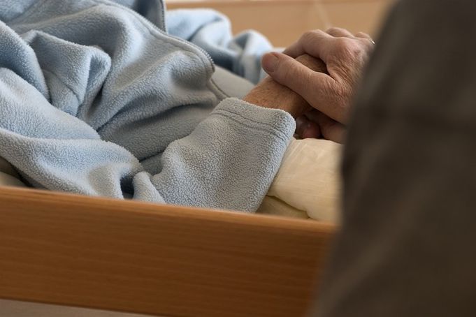 Hand einer Person hält die Hand einer im Bett liegenden Person