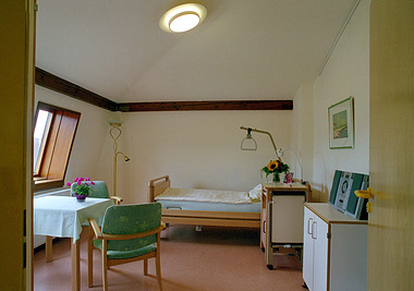Zimmer mit Einzelbett, Tisch, Stuhl, Fenster und Blumenvase