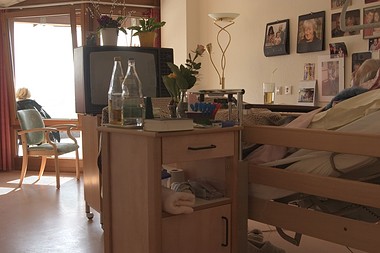 Zimmer mit Pflegebett, Nachttisch, Wasserflaschen und Familienfotos