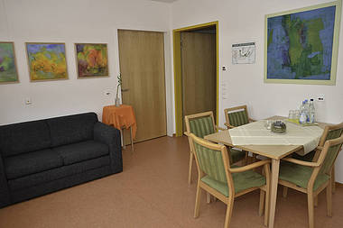 Raum mit Sofa, Esstisch, sechs Stühlen und Wandbildern