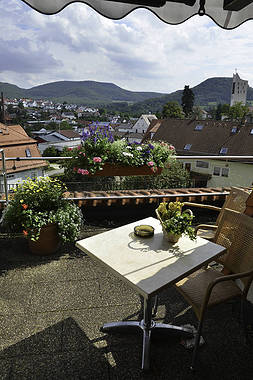 Balkon mit Tisch und Stuhl, Blumenkästen und Dorfpanorama